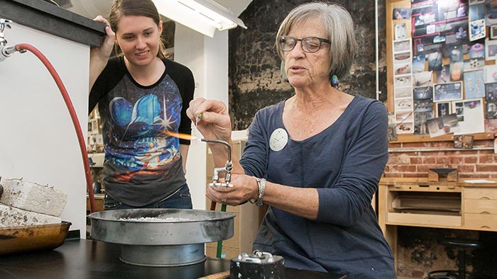 An instructor conducts hands-on experimental lab research by showing a student how to use lab equipment with an open flame.